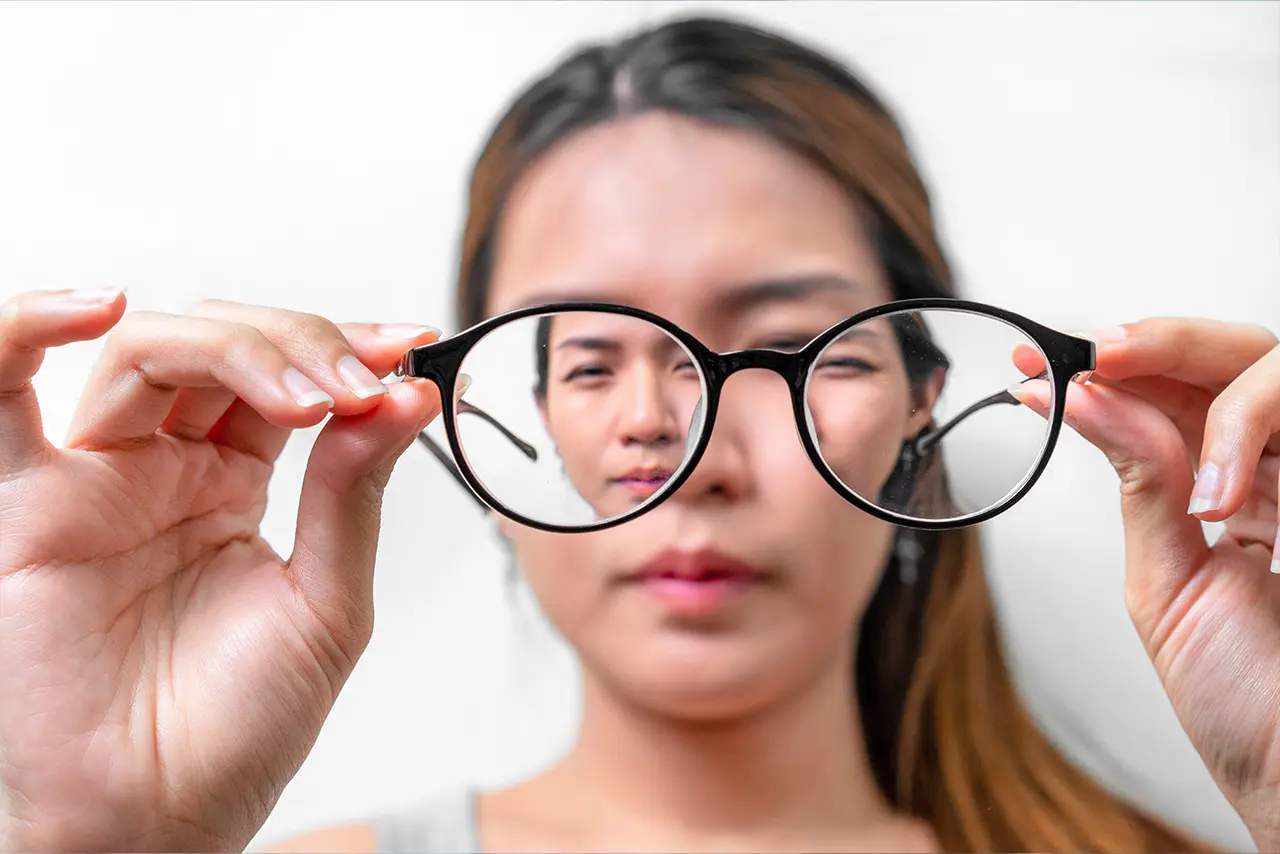 A woman holding her eyeglasses, illustrating a myopia (short-sightedness) condition.