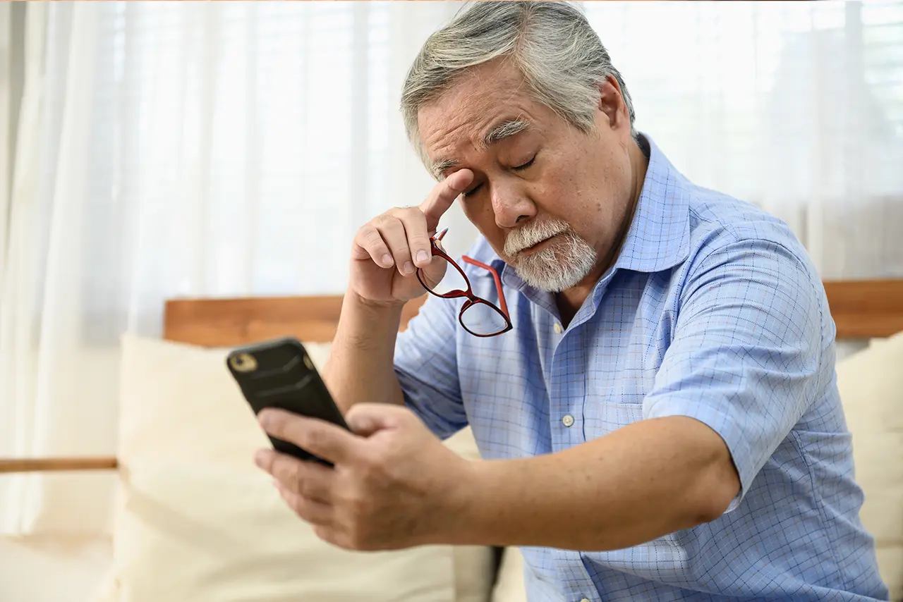 Senior man experiencing eye strain and fatigue while using a mobile phone.