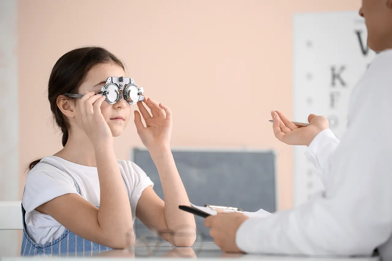 A young girl undergoing a pediatric eye exam using a trial lens frame