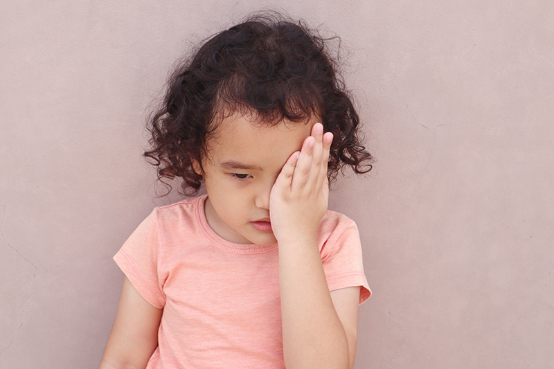 Young child covering one eye while trying to see clearly.